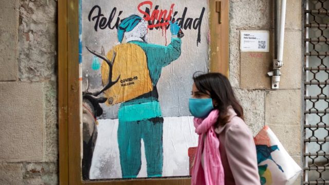 A woman walks past a new work by Italian street artist TvBoy depicting Santa Claus carrying the Covid-19 vaccine in his sack