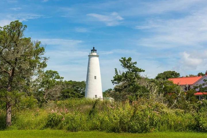 Ocracoke lighthouse on a summer morning with green marsh and red-roofed lighthouse keeper's house.