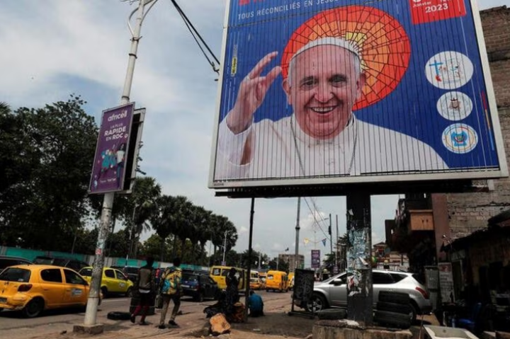 People walk next to the billboard of Pope Francis a day ahead of his arrival in Kinshasa, Democratic Republic of Congo January 30, 2023. R