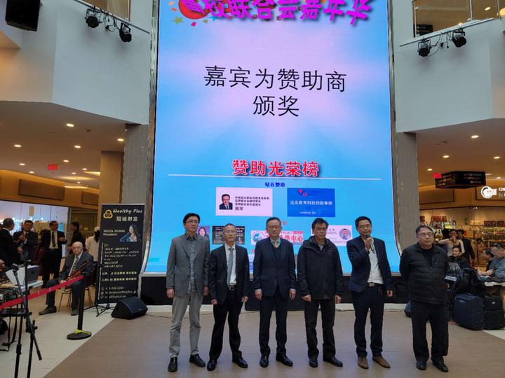 A group of men standing in front of a large screenDescription automatically generated