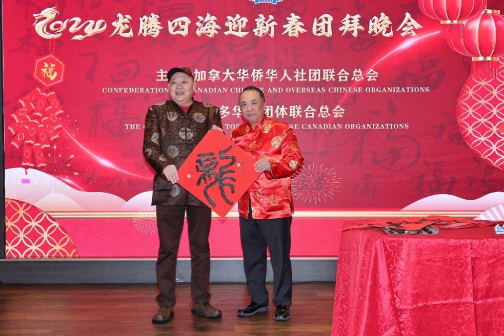 Two men standing on a stage holding a red sign

Description automatically generated