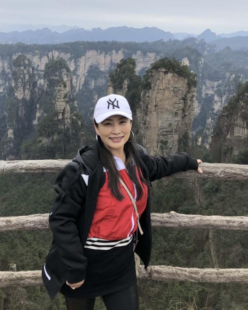 A person standing on a wooden railing with mountains in the background

Description automatically generated