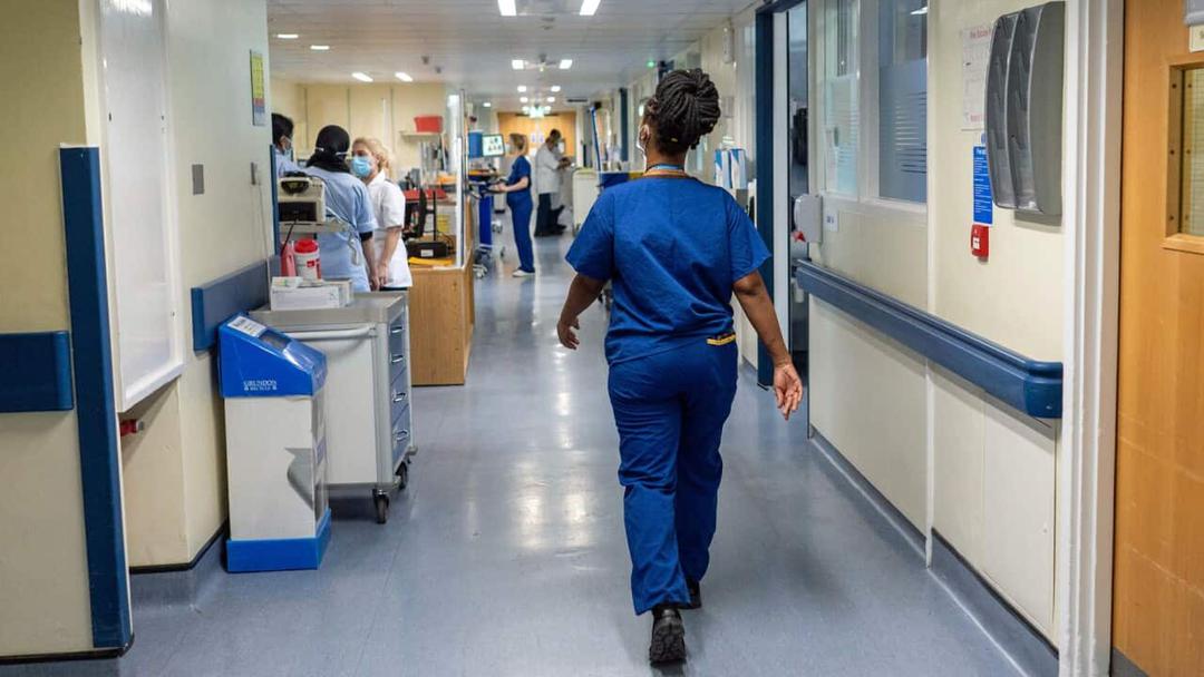 A nurse in blue medical scrubs walks down the corridor of a hospital