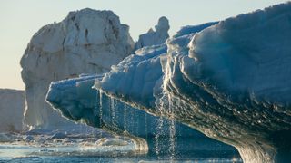 近距离拍摄冰川，融化的水流入下方的水中。其他破裂的冰川矗立在后面，映衬着苍白的天空