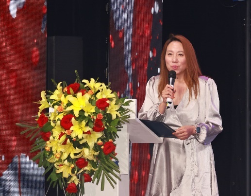 A person standing at a podium holding a microphone and holding flowers Description automatically generated