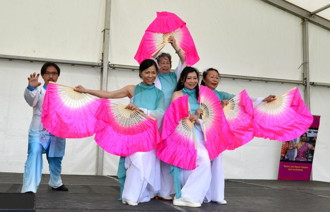 A group of people dancing with pink fans

Description automatically generated