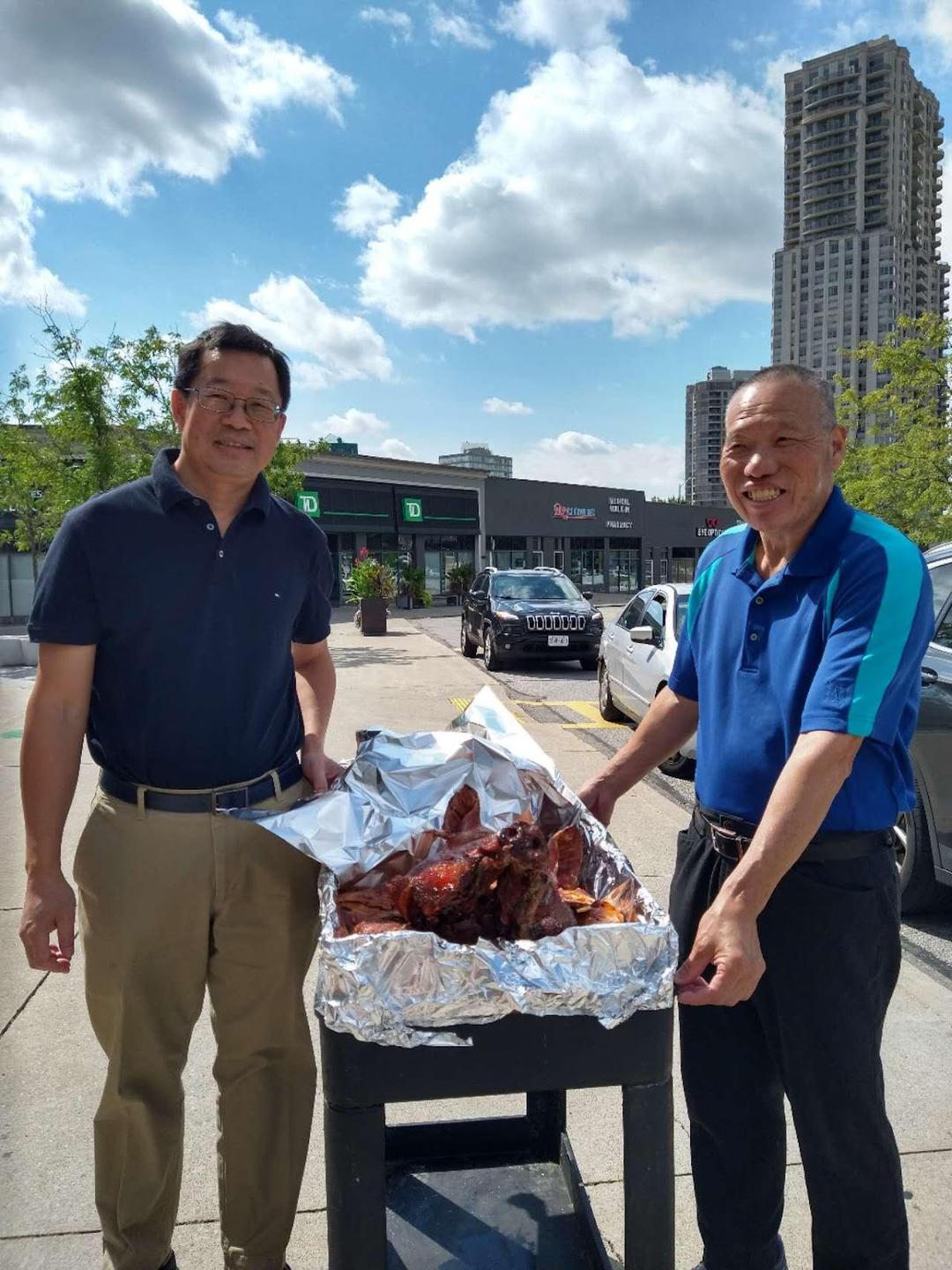 Two men standing next to a barbecueDescription automatically generated