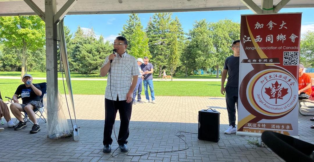 A person standing on a brick surface with a microphone in front of a group of peopleDescription automatically generated