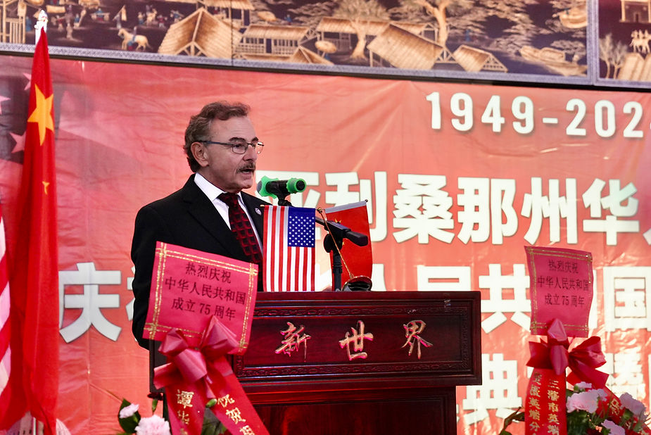 A person standing at a podium with flags and a flag behind him

Description automatically generated