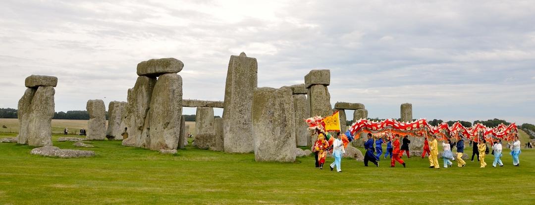 A group of people walking in a grassy field with Stonehenge in the background

Description automatically generated