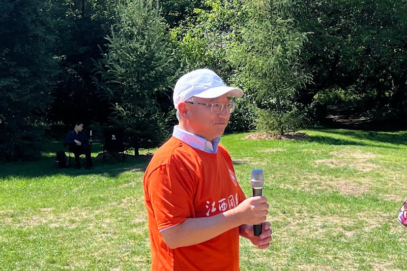 A person in a white hat holding a microphone in a parkAI-generated content may be incorrect.