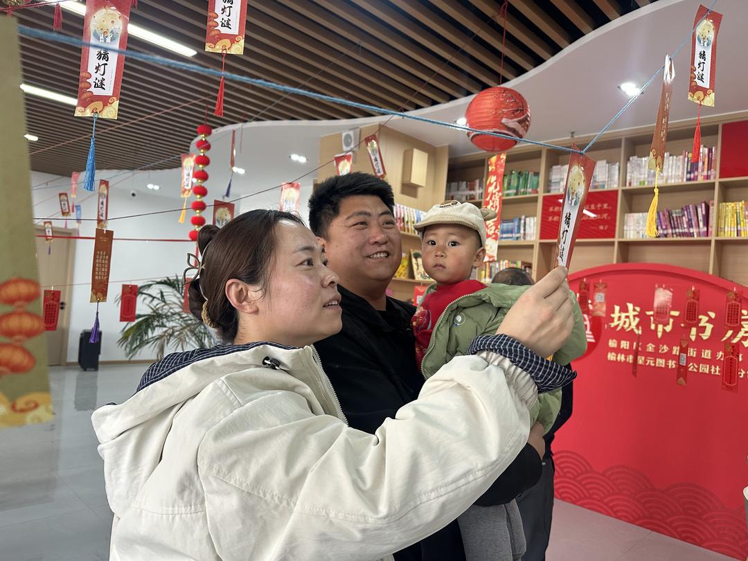 一家三口共同驻足猜灯谜,在温馨互动中乐享元宵时光