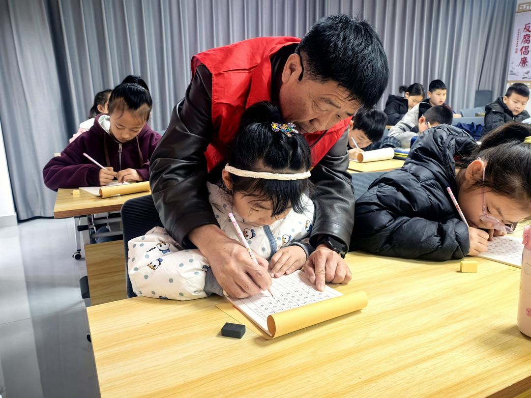 老师俯身手把手指导孩子规范握笔、练习运笔